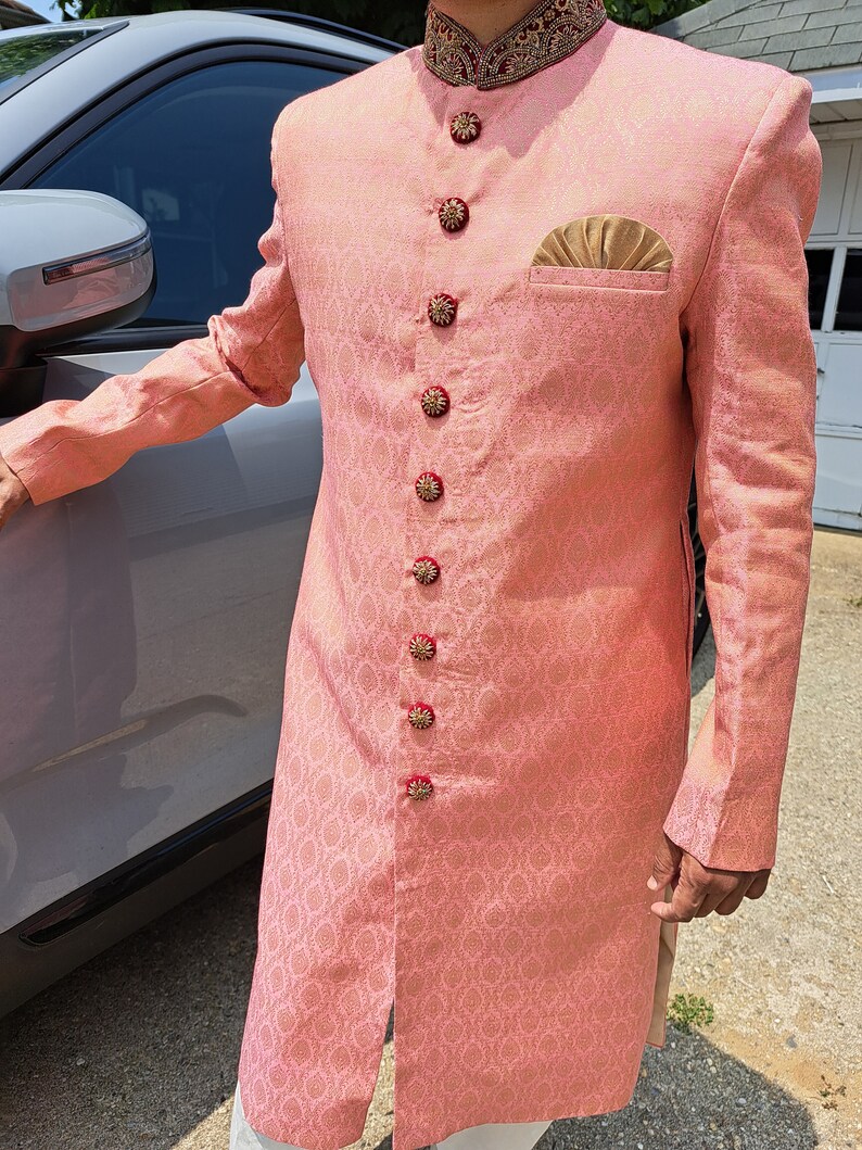 Puede incluir: Chaqueta de manga larga de color melocot&oacute;n claro con un patr&oacute;n floral detallado. La chaqueta presenta botones decorativos, un pa&ntilde;uelo de bolsillo dorado y un cuello detallado. La chaqueta forma parte de un atuendo formal tradicional.