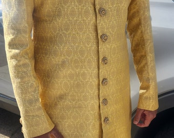 Könnte beinhalten: Eine goldgelbe, langärmlige Jacke mit Muster, verzierten Knöpfen und einem Einstecktuch. Die Jacke hat einen hohen Kragen mit goldener Stickerei. Das Kleidungsstück ist Teil eines traditionellen südasianischen Outfits.
