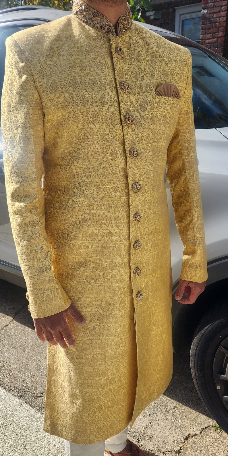 K&ouml;nnte beinhalten: Eine goldgelbe, lang&auml;rmlige Jacke mit Muster, verzierten Kn&ouml;pfen und einem Einstecktuch. Die Jacke hat einen hohen Kragen mit goldener Stickerei. Das Kleidungsst&uuml;ck ist Teil eines traditionellen s&uuml;dasianischen Outfits.