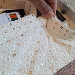 Puede incluir: Camisa blanca de algod&oacute;n con un delicado patr&oacute;n bordado y un cuello alto. El cuello tiene un ribete dorado y el texto "LELEGANT WE" es visible en la etiqueta.