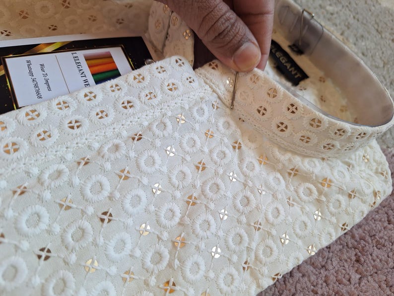 Puede incluir: Camisa blanca de algod&oacute;n con un delicado patr&oacute;n bordado y un cuello alto. El cuello tiene un ribete dorado y el texto "LELEGANT WE" es visible en la etiqueta.