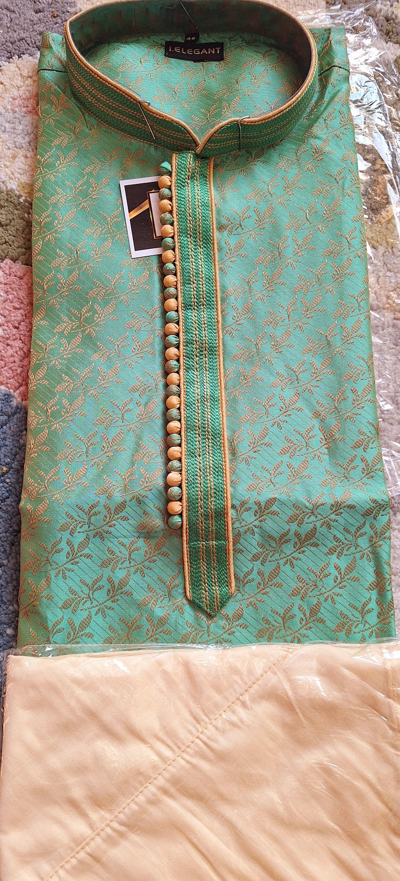 May include: A mint green kurta pajama set with a gold floral pattern. The kurta features a mandarin collar and a decorative strip with wooden beads. The label reads "I.ELEGANT".