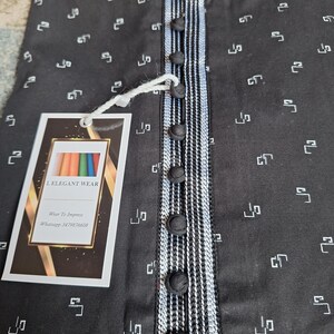 May include: Black button-down shirt with a white and black striped accent on the placket and collar. The shirt has a repeating white geometric pattern. A tag with the text "L. ELEGANT WEAR" is attached.