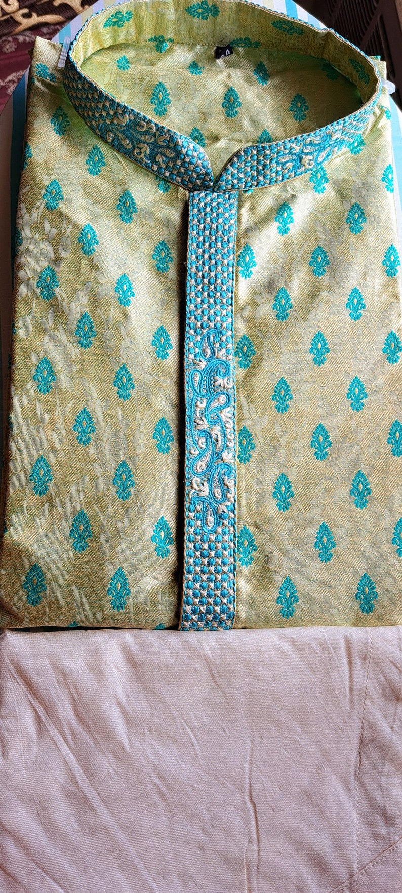 Op de afbeelding: Een lichtgroene kurta met een blauwe en witte geborduurde rand. De kurta heeft een traditioneel Indiaas ontwerp en is gemaakt van een zijdeachtige stof.