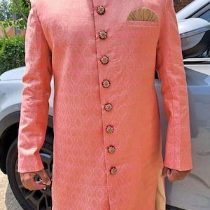 Puede incluir: Chaqueta coral de manga larga con un patr&oacute;n floral detallado. La chaqueta presenta botones dorados decorativos con detalles en rojo, un pa&ntilde;uelo de bolsillo dorado y un cuello detallado con bordados dorados y burdeos. Parte de un conjunto de ropa formal.