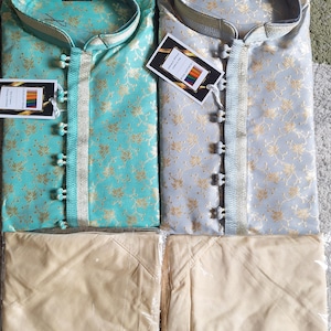 May include: Two sets of traditional Indian clothing, each set includes a long-sleeved shirt with a floral pattern and a pair of matching pants. One shirt is turquoise blue with gold floral accents, the other is light gray with gold floral accents. Both sets of pants are a light beige color.