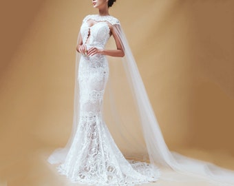 May include: A white lace wedding dress with a long train and a sheer cape. The dress has a fitted bodice and a flowing skirt.