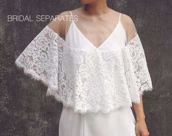 May include: A white lace bridal top with a sheer overlay and a matching white skirt. The top has a V-neckline and short, wide sleeves. The skirt is a simple, flowing style.