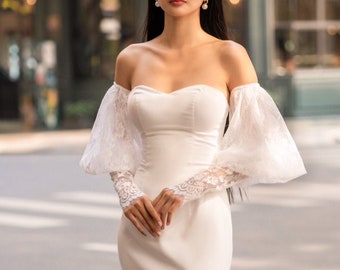 May include: A white off-the-shoulder bridal gown with long, puffy sleeves and a fitted bodice. The gown has a mermaid silhouette and a lace trim on the sleeves.
