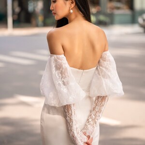 May include: A white off-the-shoulder bridal gown with long, puffy lace sleeves. The gown has a fitted bodice and a flowing skirt.