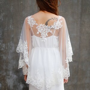 May include: A white lace overlay with a sheer fabric and a delicate floral design. The overlay is worn over a white dress.
