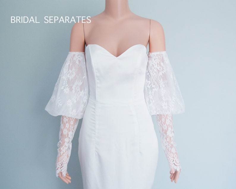 May include: White off-the-shoulder bridal dress with lace sleeves. The dress has a sweetheart neckline and a fitted silhouette. "BRIDAL SEPARATES" is written in the top left corner of the image.
