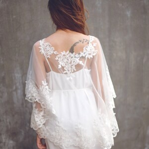 May include: A white lace overlay with a sheer fabric and a delicate floral pattern. The overlay is worn over a white dress.
