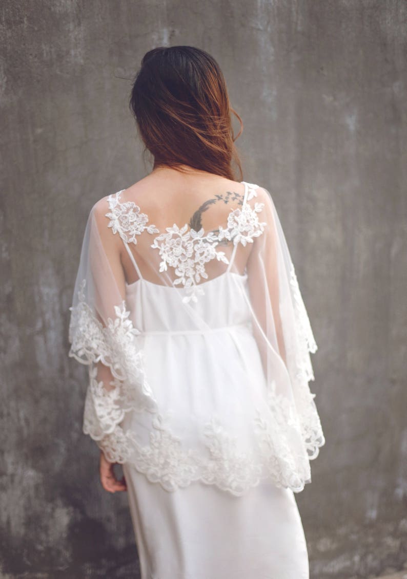 May include: A white lace overlay with a sheer fabric and a delicate floral pattern. The overlay is worn over a white dress.