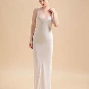 May include: A white silk slip dress with a V-neckline and thin straps. The dress is floor-length and has a simple, elegant design.  BRIDAL SEPARATES