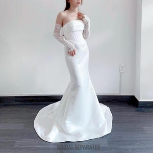 May include: A white strapless wedding dress with a fitted bodice and a flowing skirt. The dress is made of a satin fabric and has a simple, elegant design.