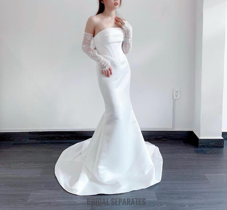 May include: A white strapless wedding dress with a fitted bodice and a flowing skirt. The dress is made of a satin fabric and has a simple, elegant design.