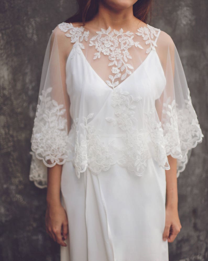 May include: A white lace overlay with a scalloped edge. The overlay is sheer and has a delicate floral pattern. It is worn over a white dress.
