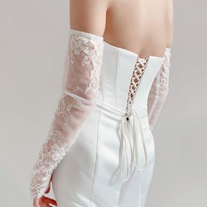 May include: White off-the-shoulder bridal gown with a lace bodice and a satin skirt. The gown features a lace-up back with a bow.