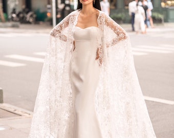 May include: A white bridal gown with a lace overlay and a long train. The gown has a strapless sweetheart neckline and a fitted bodice. The lace overlay is sheer and has a delicate floral pattern.