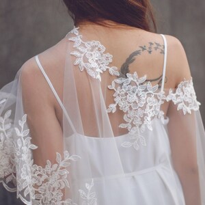 May include: A white lace bridal shawl with delicate floral patterns. The shawl is sheer and lightweight, perfect for adding a touch of elegance to a wedding dress.