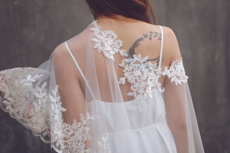 May include: A white lace bridal shawl with delicate floral patterns. The shawl is sheer and lightweight, perfect for adding a touch of elegance to a wedding dress.