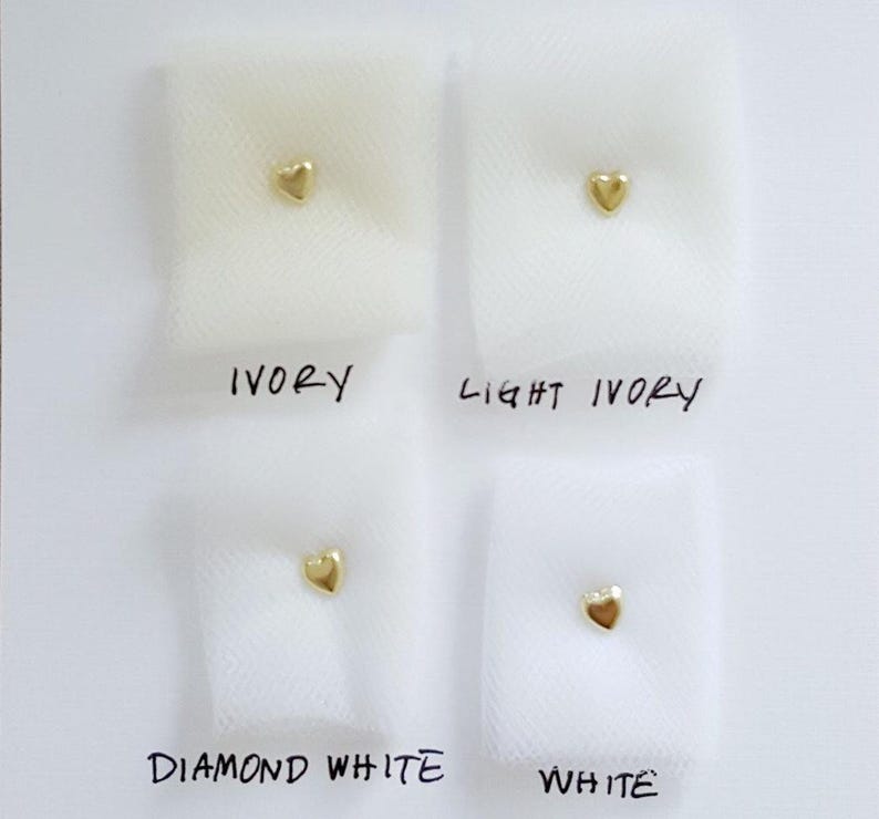May include: Four swatches of fabric in ivory, light ivory, diamond white, and white. Each swatch has a small gold heart shape placed on it.