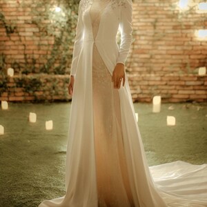 May include: A white bridal gown with a long train and a high neckline. The gown has a sheer overlay with sparkling embellishments and a fitted bodice.
