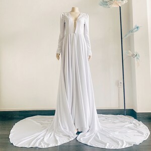 May include: A white long-sleeved gown with a plunging neckline and a flowing skirt. The gown has a beaded detail at the neckline.