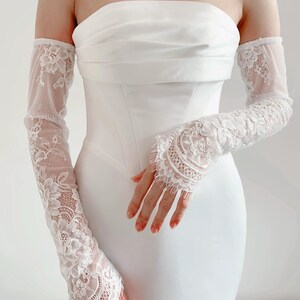May include: White lace bridal gloves with a delicate floral pattern. The gloves extend to the elbow and are made of a sheer fabric.