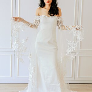 May include: A white off-the-shoulder wedding dress with a fitted bodice and a flowing skirt. The dress features delicate lace detailing on the sleeves and hem.