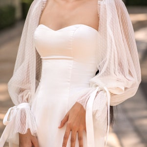 May include: A white bridal separates dress with a sweetheart neckline and long, puffy sleeves with lace detailing. The sleeves have a tie at the wrist.