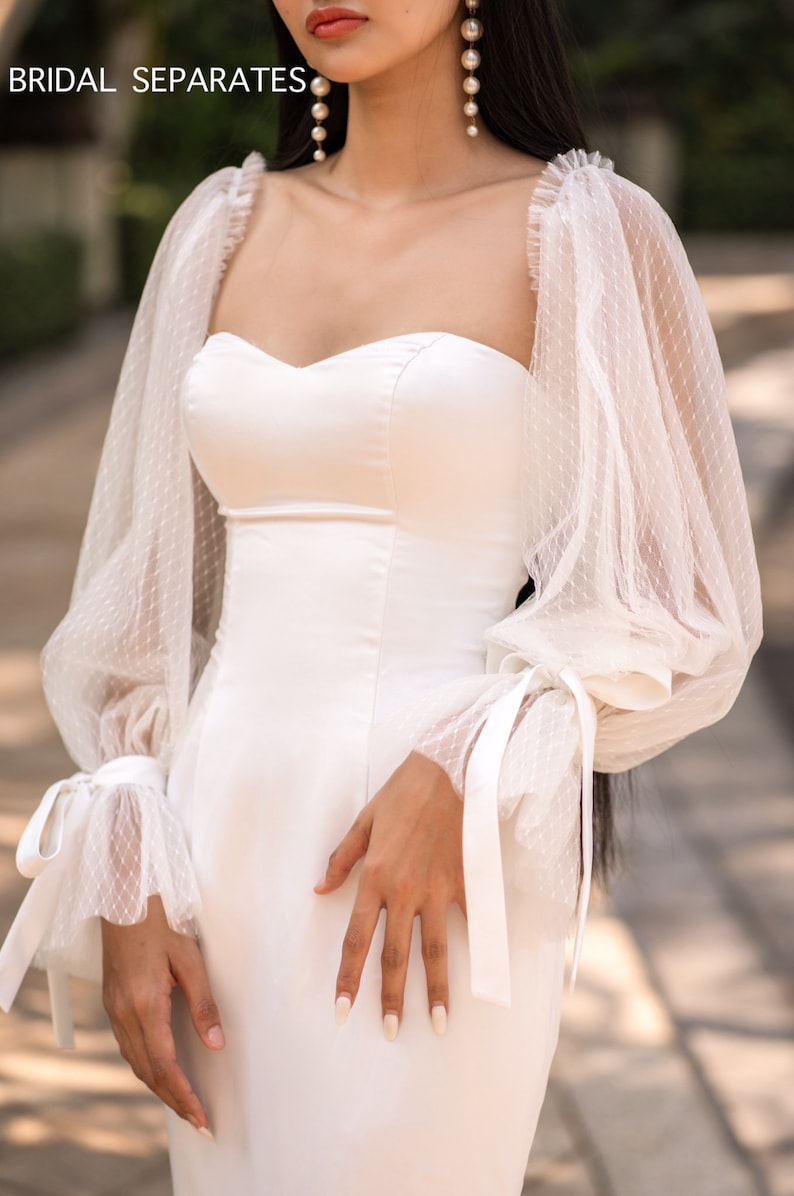 May include: A white bridal separates dress with a sweetheart neckline and long, puffy sleeves with lace detailing. The sleeves have a tie at the wrist.