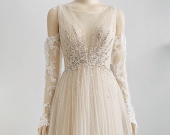 May include: A sheer, off-the-shoulder wedding dress with a beaded bodice and a flowing tulle skirt. The dress is paired with delicate lace sleeves. The text "BRIDAL SEPARATES" is visible at the bottom of the image.