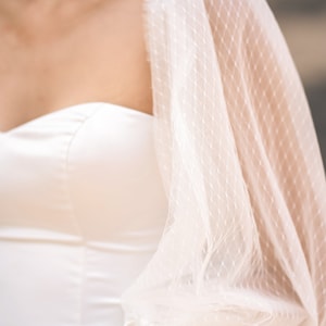 May include: A white strapless dress with a sheer, dotted overlay and a bow at the waist.