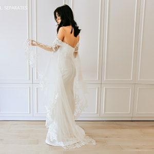 May include: A white off-the-shoulder bridal gown with long, sheer sleeves featuring delicate lace detailing. The gown has a fitted bodice and a flowing skirt.