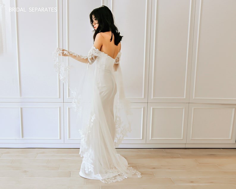 May include: A white off-the-shoulder bridal gown with long, sheer sleeves featuring delicate lace detailing. The gown has a fitted bodice and a flowing skirt.