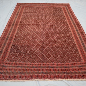 May include: A rectangular, hand-woven rug with a diamond pattern in shades of red and brown. The rug has a detailed border with geometric designs and a fringed edge. The overall design is symmetrical and traditional.