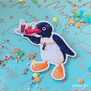 Puede incluir: Un personaje de dibujos animados de pingüino azul y blanco que lleva un delantal blanco con la palabra "NOOTERS" impresa en él. El pingüino sostiene una bandeja con tres vasos de té helado. El fondo es una superficie azul claro con un patrón blanco y dorado.