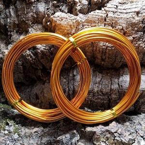 May include: Two spools of gold-colored wire, wrapped around each other, on a rough, brown, textured surface.