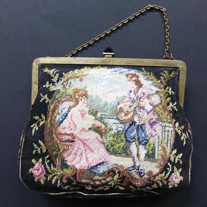 Könnte beinhalten: Eine vintage Abendtasche in Schwarz und Gold mit einer Kettenkette. Die Tasche ist mit einer bunten Szene eines Paares in einem Garten bestickt.