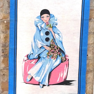 Könnte beinhalten: Ein vintage Küchenhandtuch mit blauem Rand und weißem Hintergrund. Das Design zeigt eine Frau in einem blau-weißen Narrenkostüm, die einen Strauß rosa Rosen hält. Sie sitzt auf einem rosa Kissen.