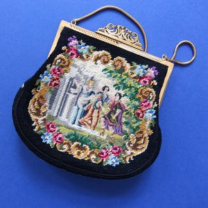 Könnte beinhalten: Eine vintage Abendtasche aus schwarzem Samt mit einem goldenen Kettenhenkel und einer floralen Stickerei mit drei Figuren in einem Garten.