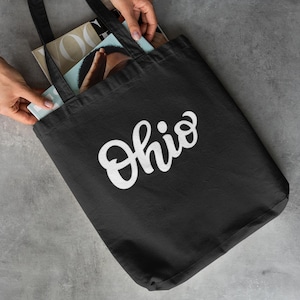 May include: Black tote bag with white text that says "Ohio". The bag is filled with magazines.