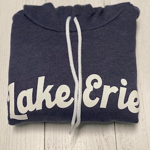 Peut inclure: Un sweat à capuche bleu marine avec un cordon de serrage blanc et le texte "Lake Erie" en blanc sur le devant.