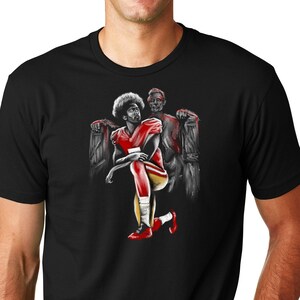 May include: A black t-shirt with a graphic print of a football player kneeling with another player standing behind him. The graphic is in shades of gray, red, and yellow.