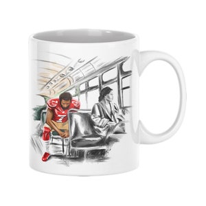 May include: White ceramic mug with a black and white illustration of a football player and a woman sitting on a bus. The football player is wearing a red jersey with a white number 7. The woman is wearing a white coat. The bus is drawn in a sketchy style.