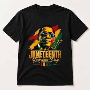 May include: Black t-shirt featuring a graphic of a man wearing sunglasses, with the text "Juneteenth Freedom Day 1865" in gold lettering. The design includes red, yellow, and green stripes and a chain graphic.