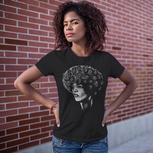 May include: A black t-shirt with a graphic of a woman with an afro hairstyle. The afro is made up of many faces, and the woman has a single tear running down her cheek.