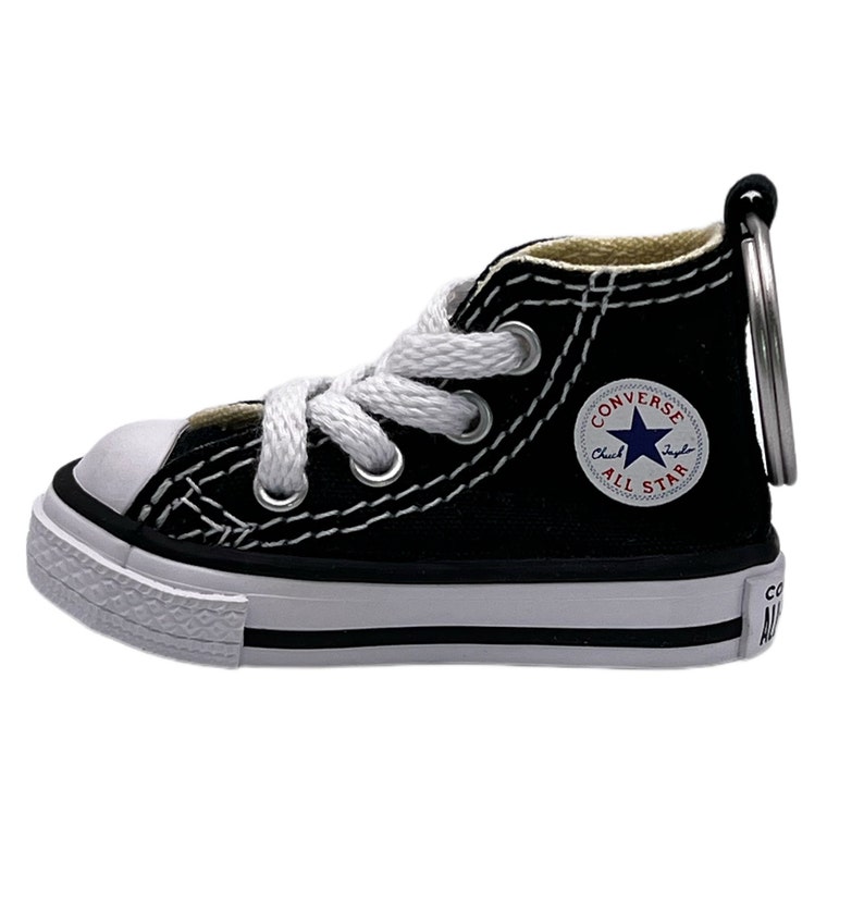 May include: Black Converse All Star high-top sneaker keychain with white laces and a red star logo. The keychain is made of durable materials and features a metal ring for attaching to keys.